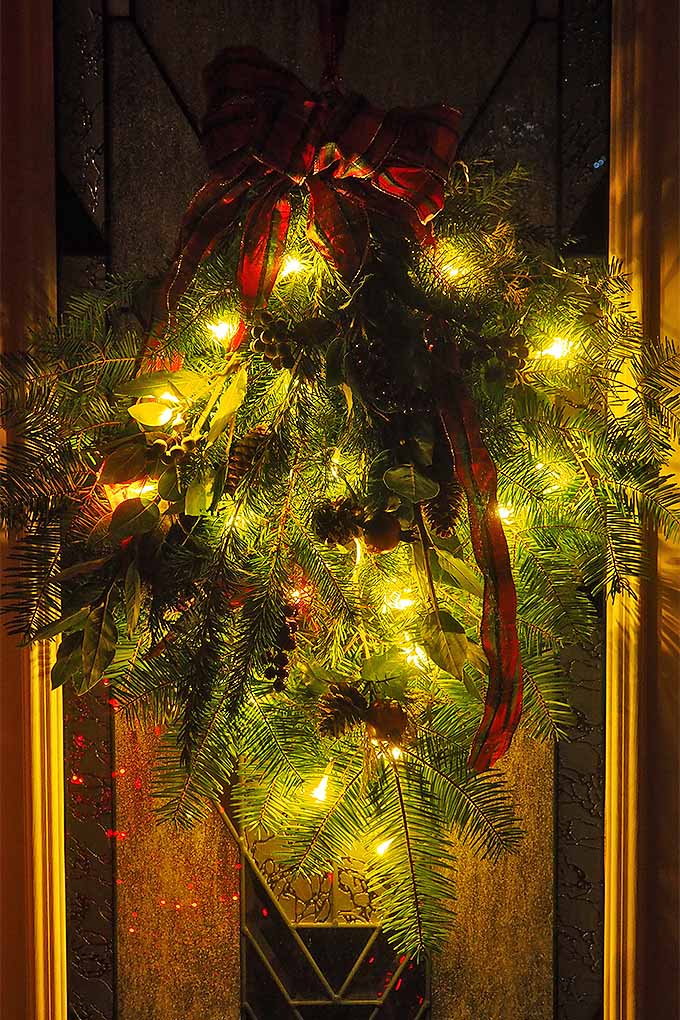 Agregue nuestro sencillo tutorial a sus planes de decoración navideña: le enseñaremos cómo hacer un botín festivo de hoja perenne para colgar en la puerta principal: 