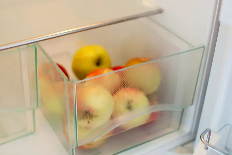 Una imagen horizontal de cerca de un montón de fruta fresca en el cajón para verduras de un refrigerador.