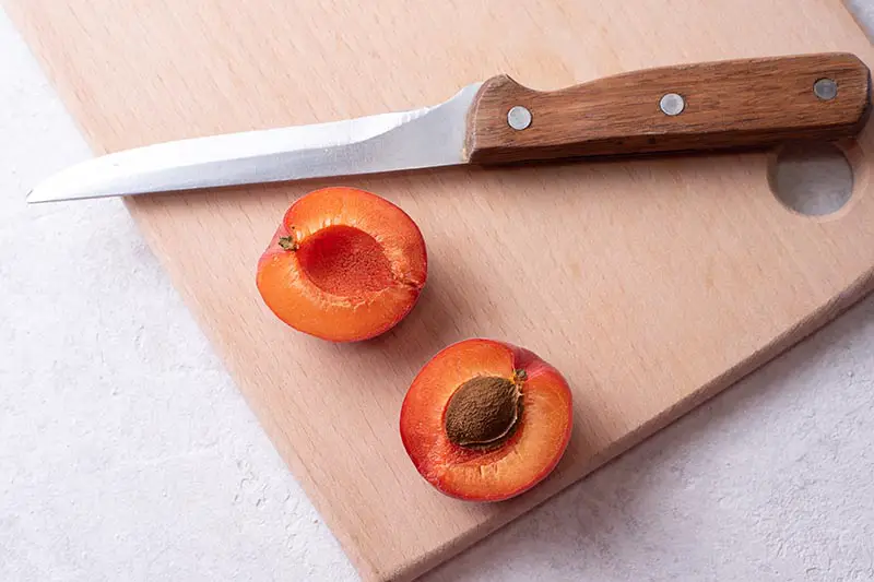 Una imagen horizontal de primer plano de un albaricoque cortado por la mitad en una tabla de cortar con un cuchillo.