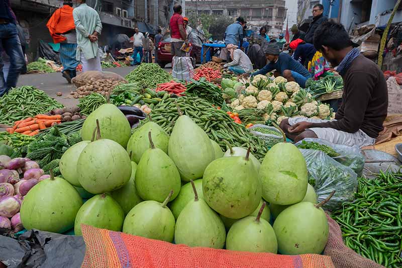 Una imagen horizontal de un mercado que vende una variedad de frutas y verduras en una calle concurrida.