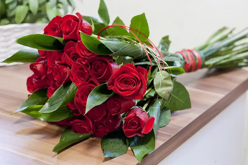 Una imagen horizontal de primer plano de un ramo de flores rojas con cintas decorativas sobre una superficie de madera.
