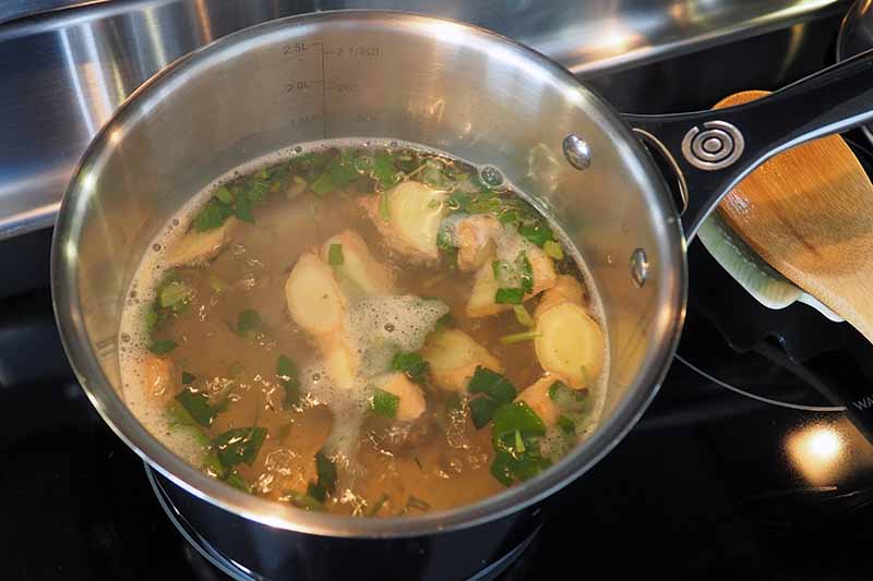 Una imagen horizontal de primer plano de una sartén con ingredientes para hacer un té de hierbas relajante en una estufa caliente.