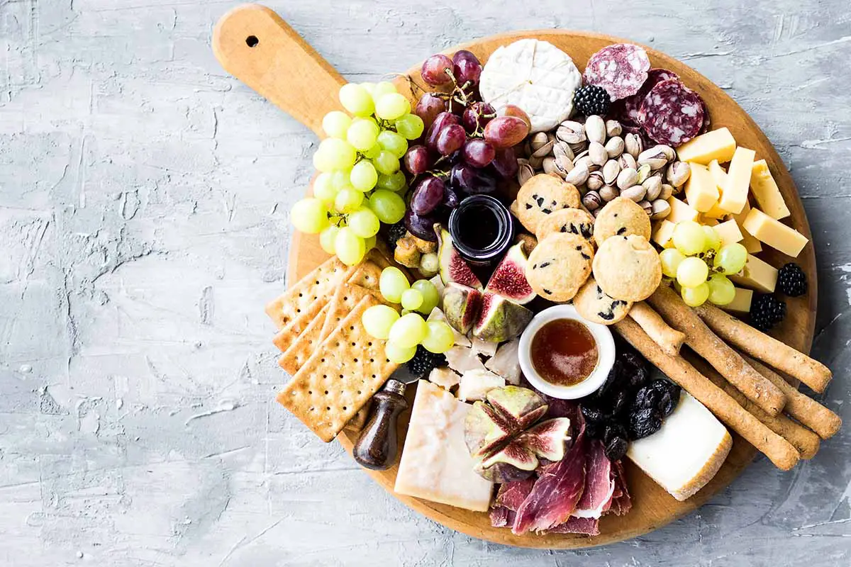 Una imagen horizontal de arriba hacia abajo de una tabla de quesos con una variedad de frutas, nueces y panes diferentes.