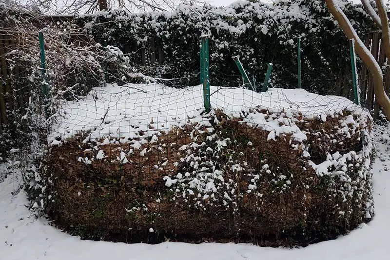 Una imagen horizontal de primer plano de una pila de abono en invierno, cubierta de nieve.