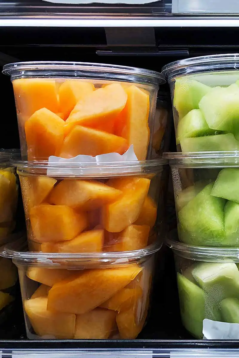 Una imagen vertical de recipientes de plástico que contienen melón fresco en cubos, almacenados en el refrigerador.