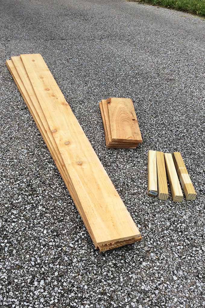 Varias piezas de madera de varios tamaños, descansando en pilas dispuestas según el tamaño en un camino de entrada asfaltado.