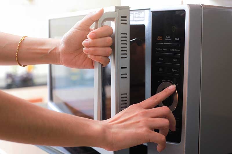 Una imagen horizontal de cerca de una mujer abriendo la puerta de un horno de microondas.
