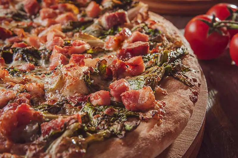 Una imagen horizontal de primer plano de una pizza casera con tomates y hierbas que es suficiente para hacer agua la boca y llamar a Domino's.