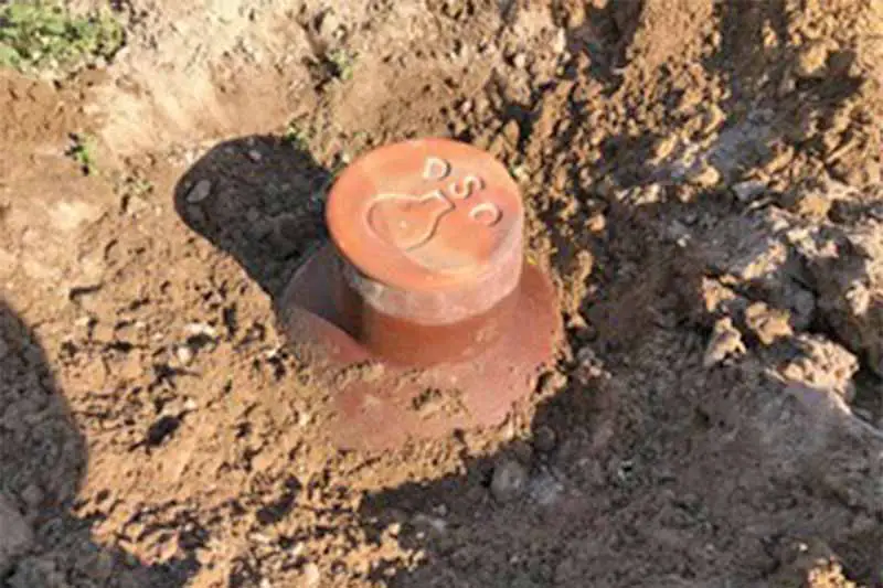 Una olla de cerámica de terracota con el cuello expuesto, enterrada en tierra marrón.