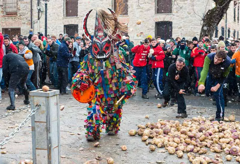 Un hombre vestido con un traje de diablo multicolor es objeto de que le arrojen nabos en la Fiesta de Jarramplas.