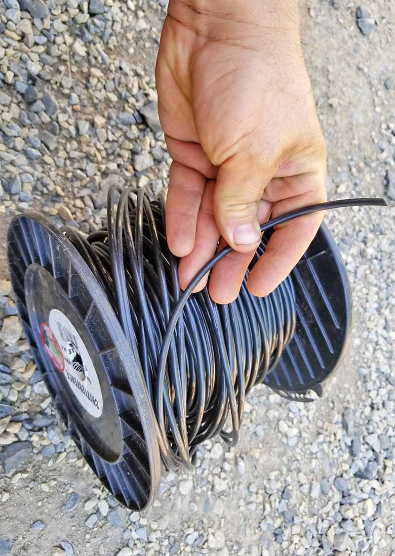 Una mano sostiene el extremo de un carrete de cable de tensión negro sobre asfalto gris.