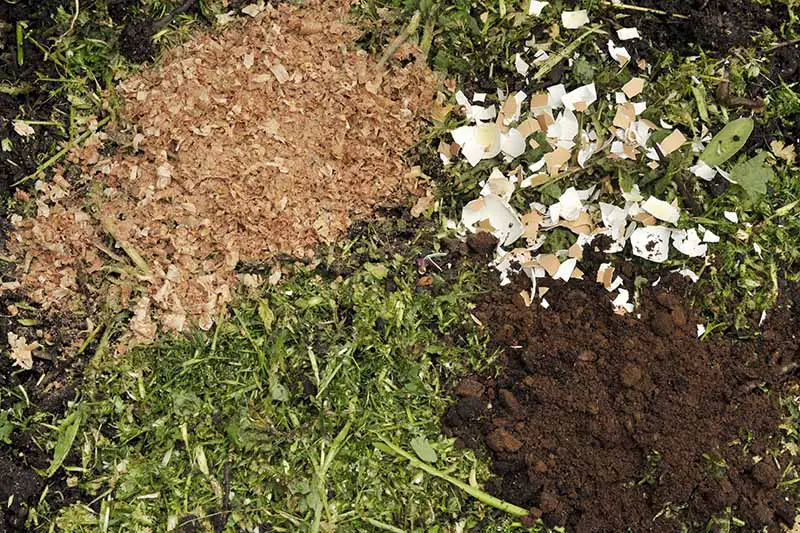 Una imagen horizontal de primer plano de posos de café, cáscaras de huevo, virutas de madera y recortes de jardín para una pila de compost.