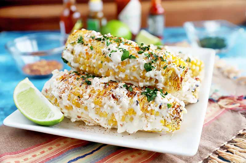 Una imagen horizontal de primer plano de maíz dulce mexicano en un plato blanco con una rodaja de limón a un lado.