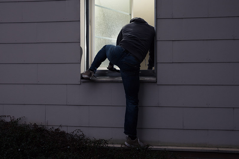 Una vista trasera de un hombre subiendo a una casa a través de la ventana en la oscuridad.