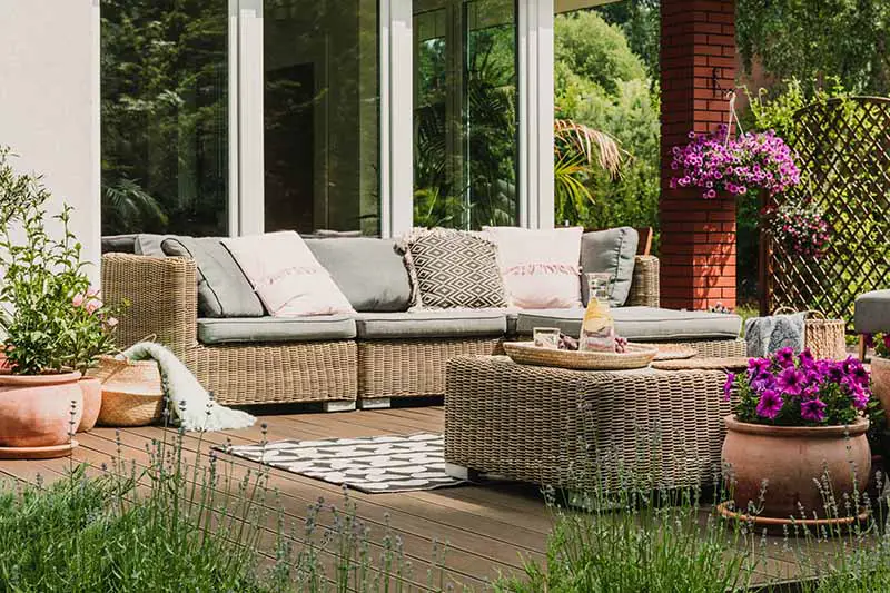 Una imagen horizontal de una terraza con muebles de mimbre, alfombras y una variedad de plantas.