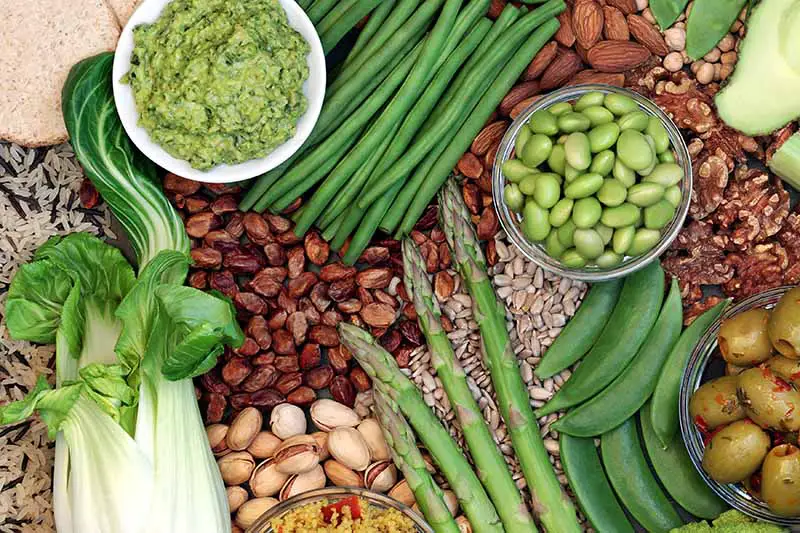 Una imagen de arriba hacia abajo de una variedad de vegetales, legumbres, nueces y semillas como parte de una dieta saludable basada en plantas.