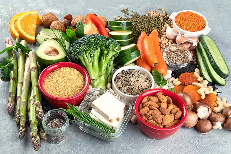 Un primer plano de una variedad de frutas, verduras y nueces, para mostrar las fuentes de proteínas de origen vegetal que se deben incluir como parte de una dieta saludable.