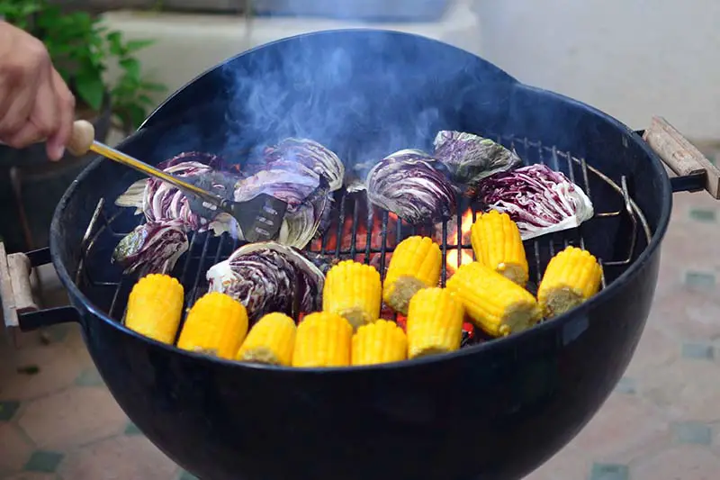 Una imagen horizontal de cerca de una parrilla de carbón cocinando cabezas de radicchio y maíz dulce.