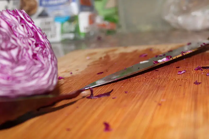 Una imagen horizontal de primer plano de la mitad de la col roja colocada sobre una tabla de cortar de madera con un cuchillo.