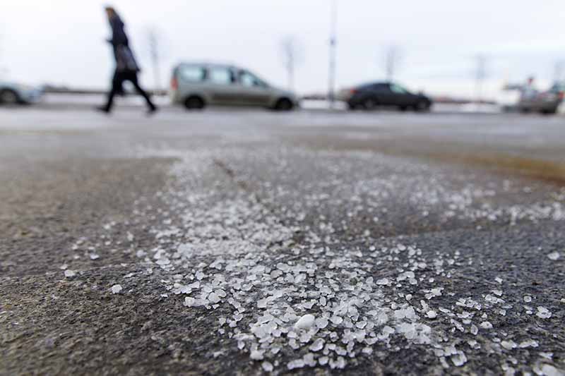 Una imagen horizontal de productos químicos descongelantes rociados en una carretera en invierno.