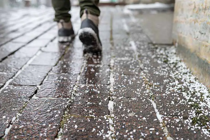 Una imagen horizontal de los pies de una persona caminando por una acera a la que se le ha aplicado sal en invierno.