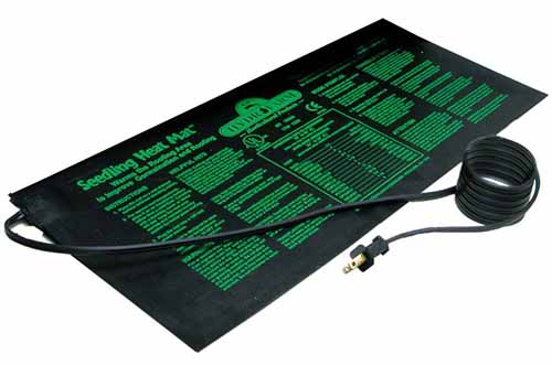 Un primer plano de una alfombrilla térmica de plástico negro con un cable eléctrico y un enchufe.  Hay escritura verde en la libreta.