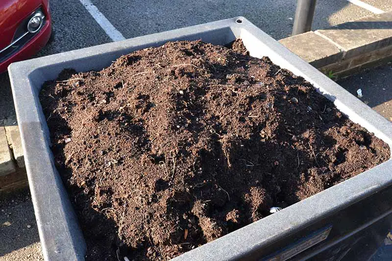 Una imagen horizontal de primer plano de una sembradora de plástico cuadrada llena de tierra lista para plantar verduras.