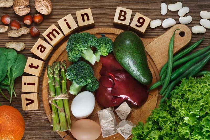 Una tabla de cortar de madera circular con una variedad de verduras y carnes fuentes de vitamina B9.  Alrededor del exterior hay un letrero de madera.